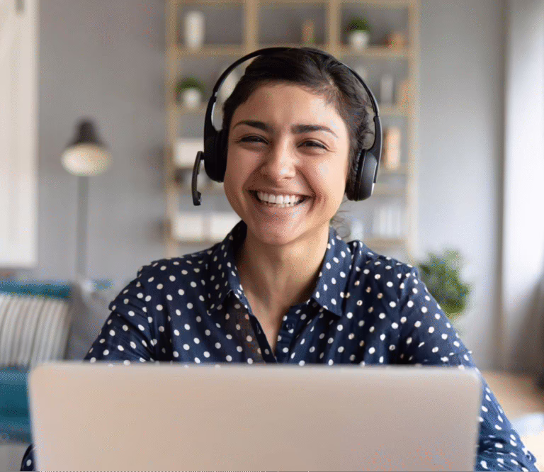A woman uses a laptop with headphones on, smiling as she enjoys her activity.
