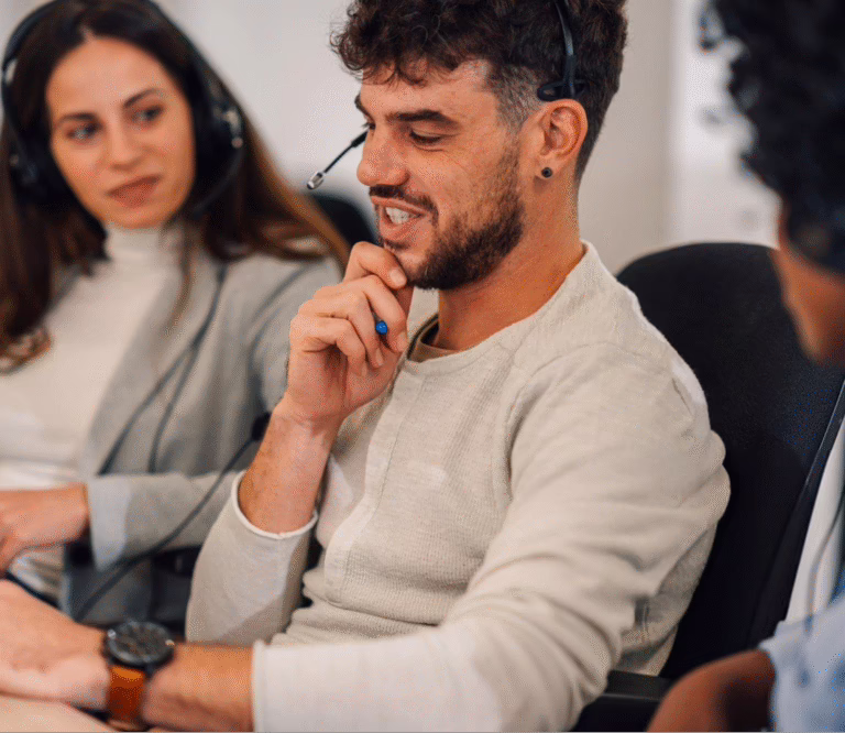 At a desk, a smiling man with headphones engages with two women who are looking at him.