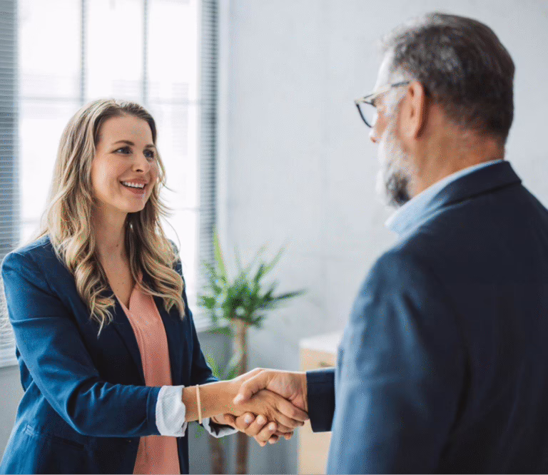 A woman and a man shaking hands in a modern office setting, symbolizing a professional agreement or partnership.